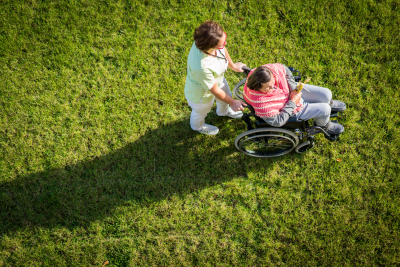 elderly woman in wheelchair top view on grass with nurse taking care of her